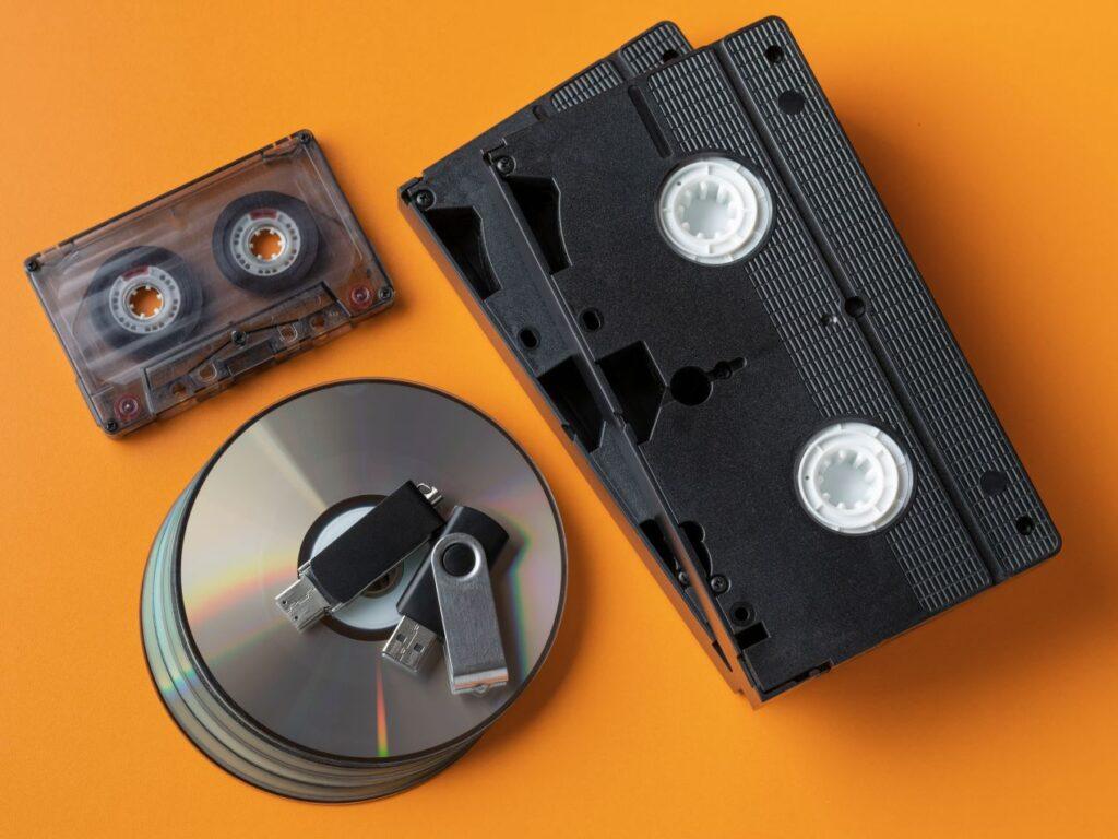 Ein Stapel VHS-Kassetten neben CDs und USB-Sticks, symbolisiert die Digitalisierung von analogen Erinnerungen.